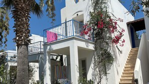 A white building with a balcony, a staircase, and a garden with flowers and a palm tree. - Eskiyali Otel (Bodrum)