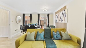 Un salon moderne avec un canapé jaune, un coin repas à l’arrière-plan et des œuvres d’art accrochées aux murs.