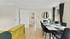 Un coin repas avec une table dressée pour quatre personnes, un banc jaune et un miroir au mur.