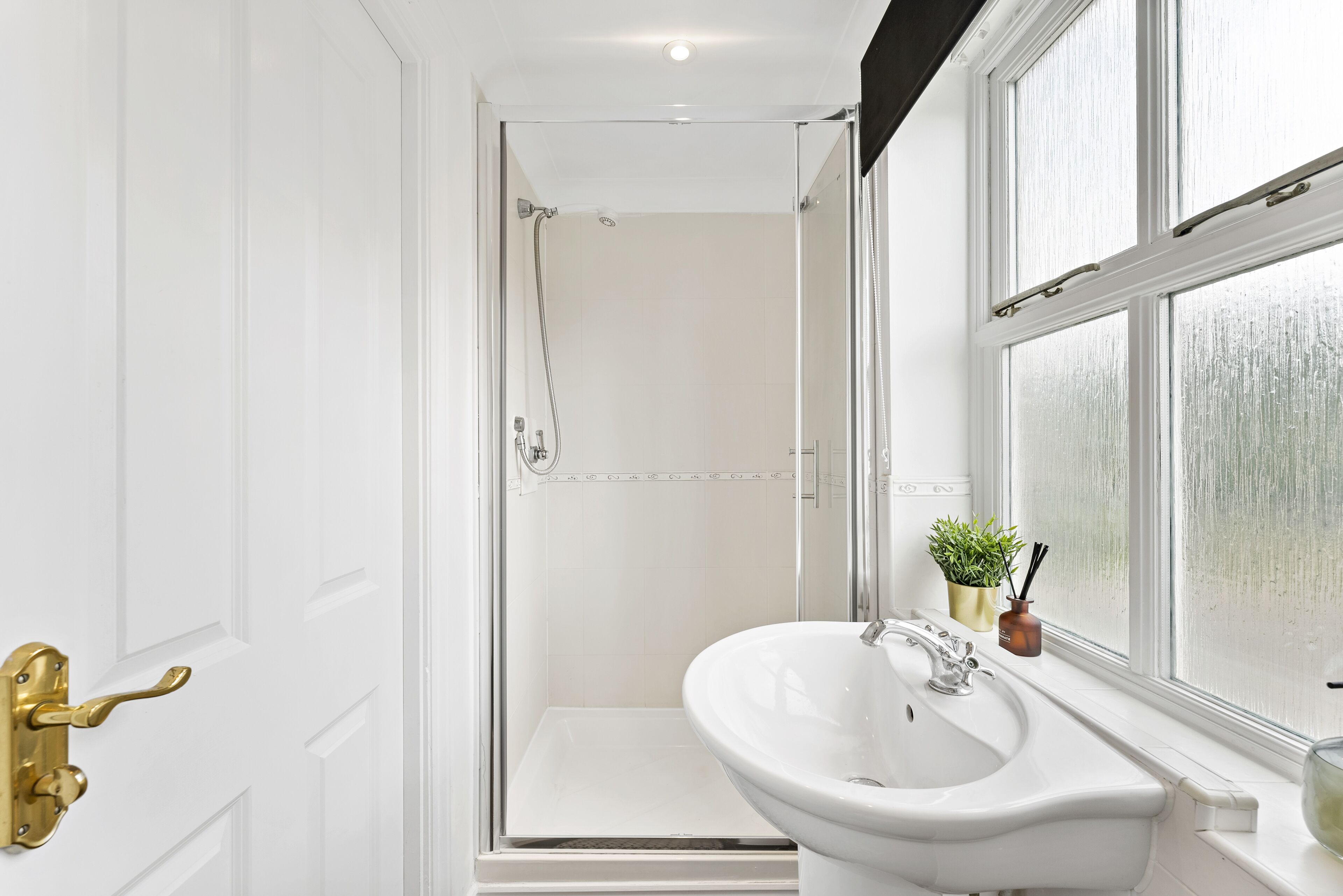 A bathroom with a shower, a sink, and a window.