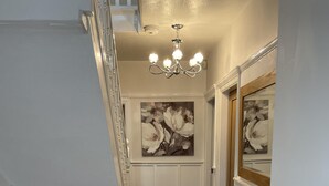 A hallway with wooden flooring, white walls, a chandelier, and two framed floral paintings.
