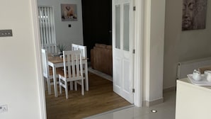 A modern living room with a white sofa, a dining area with a wooden table and chairs, and a hallway leading to another room.