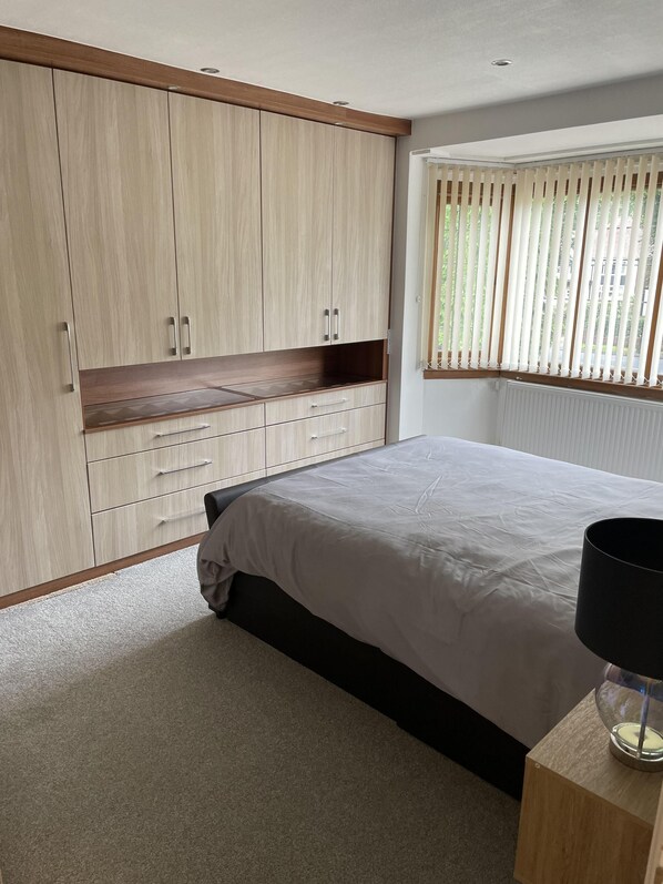 A bedroom with a bed, a nightstand, a wardrobe, and a window with blinds. - Remarkable 5-bed House in Walsall (Walsall)