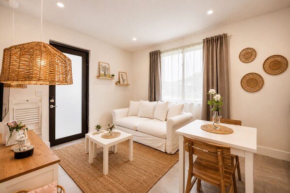 A modern living room with a white sofa, a dining table, a wicker lamp, and a window with curtains.