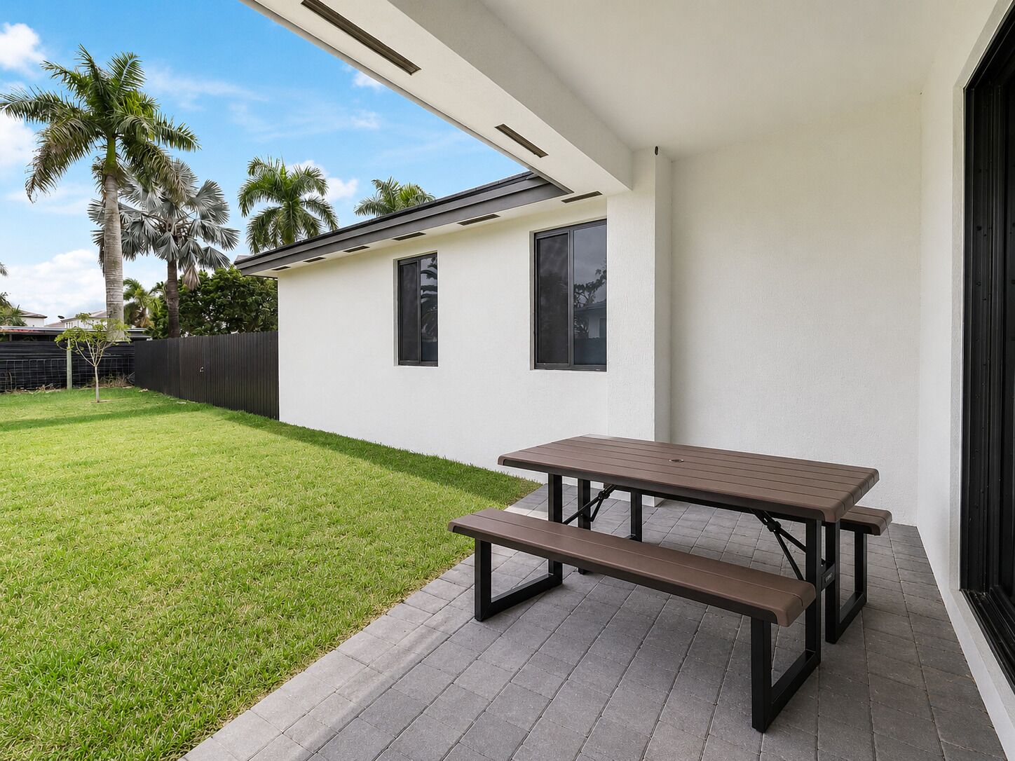 Un patio con una mesa, un banco, un edificio blanco y un jardín con palmeras.