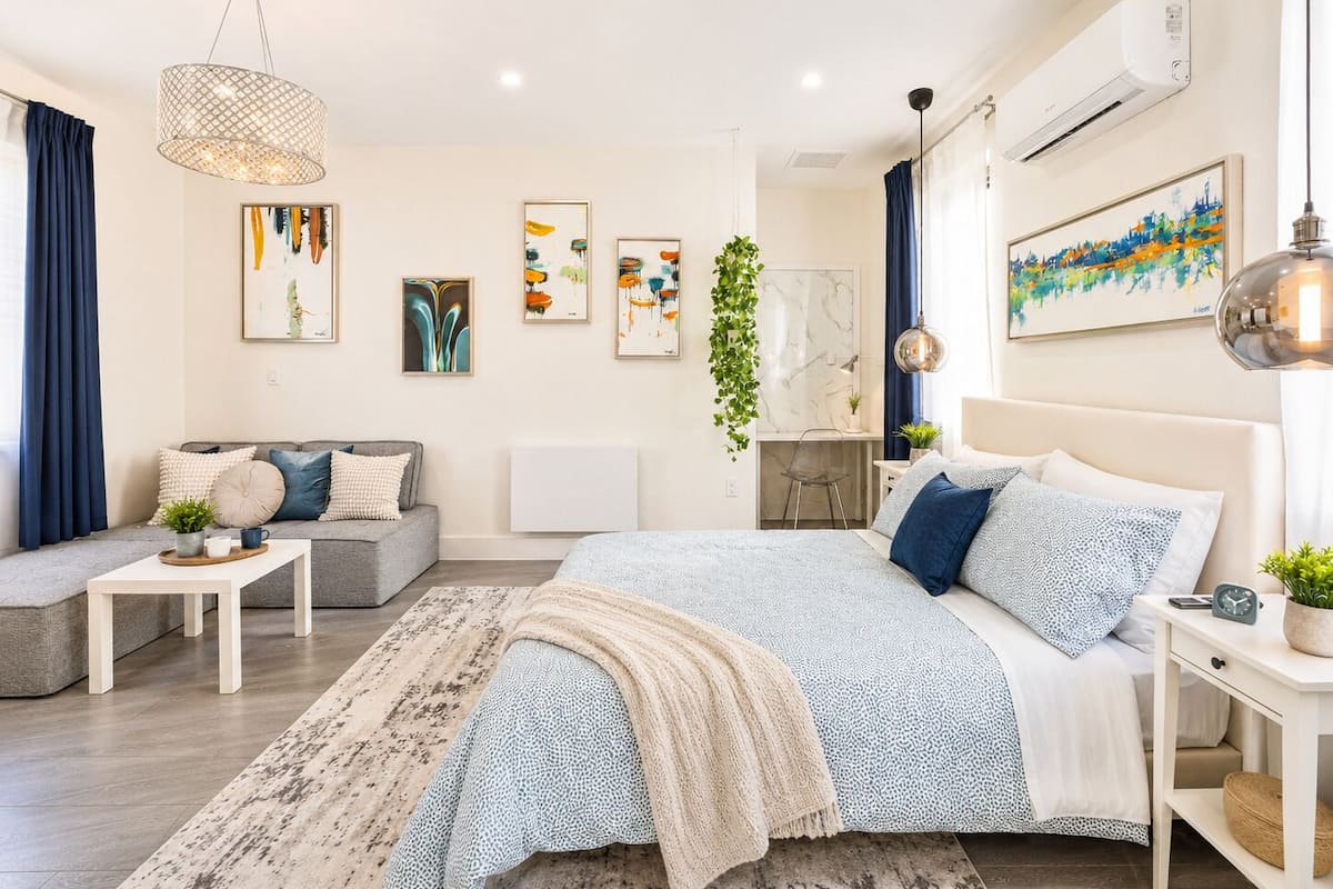 A modern bedroom with a bed, bedside tables, a desk, and a hanging plant.