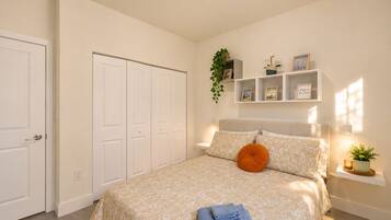 A bedroom with a bed, a nightstand, a shelf with decorative items, and a door.