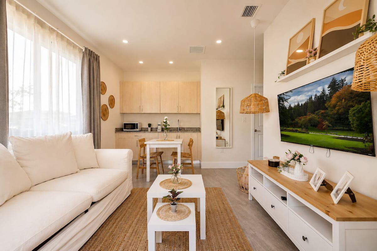 A modern living room with a sofa, a dining table, and a TV mounted on the wall.