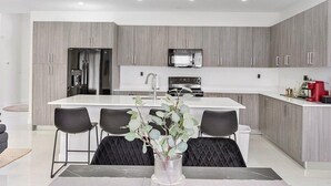 A modern kitchen with grey cabinetry, a central island with chairs, and a dining table. - Avi Lux Stay (Miami)