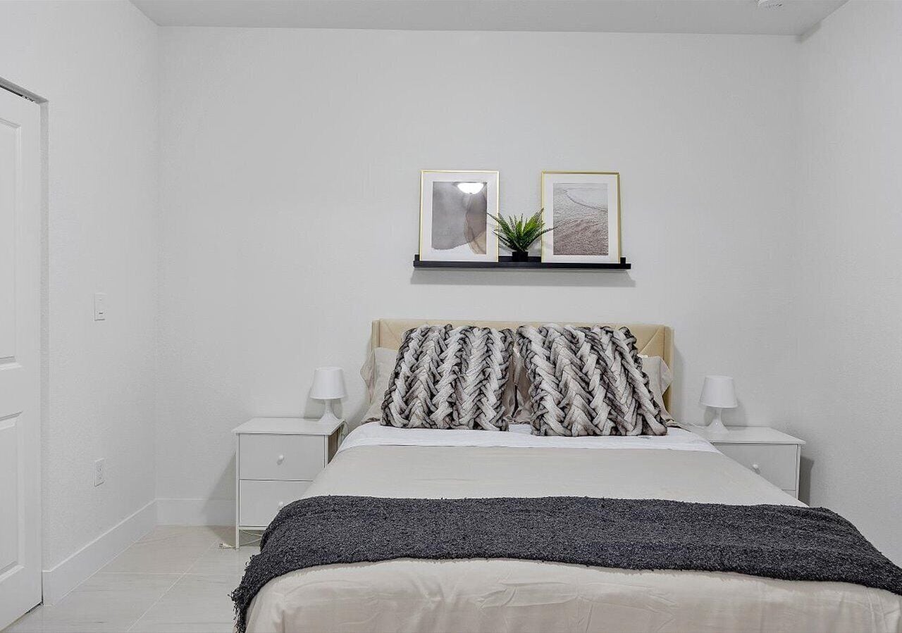 Une chambre à coucher comprenant un lit, deux tables de chevet, une commode, une étagère murale avec deux tableaux encadrés et une plante en pot.
