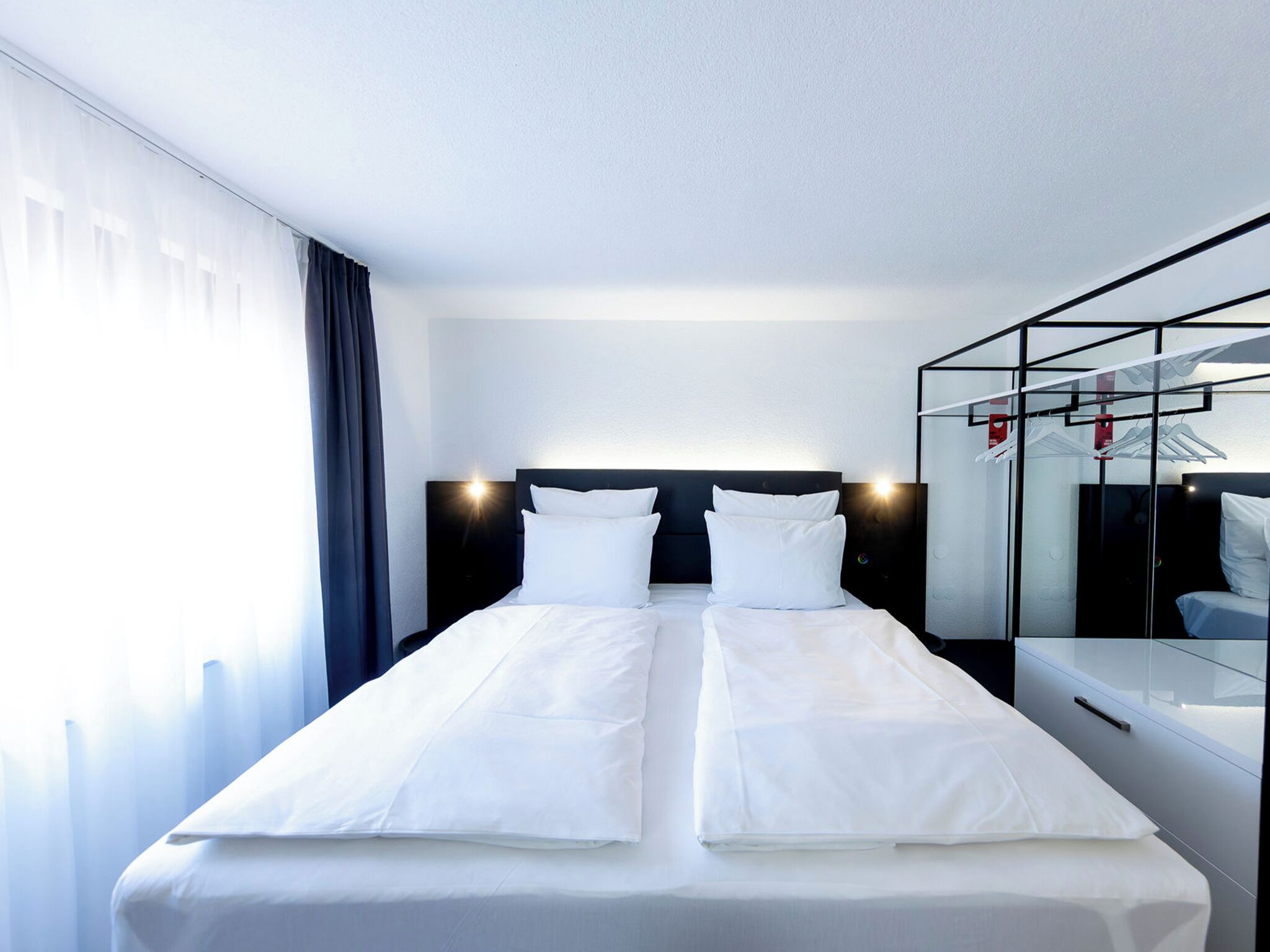 Una habitación de hotel con cama, mesita de noche, espejo y armario.