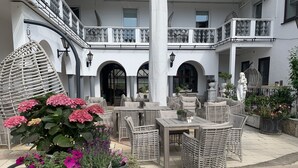 A spacious outdoor seating area with wicker furniture and potted plants. - DORMERO Hotel Aalen (Aalen)