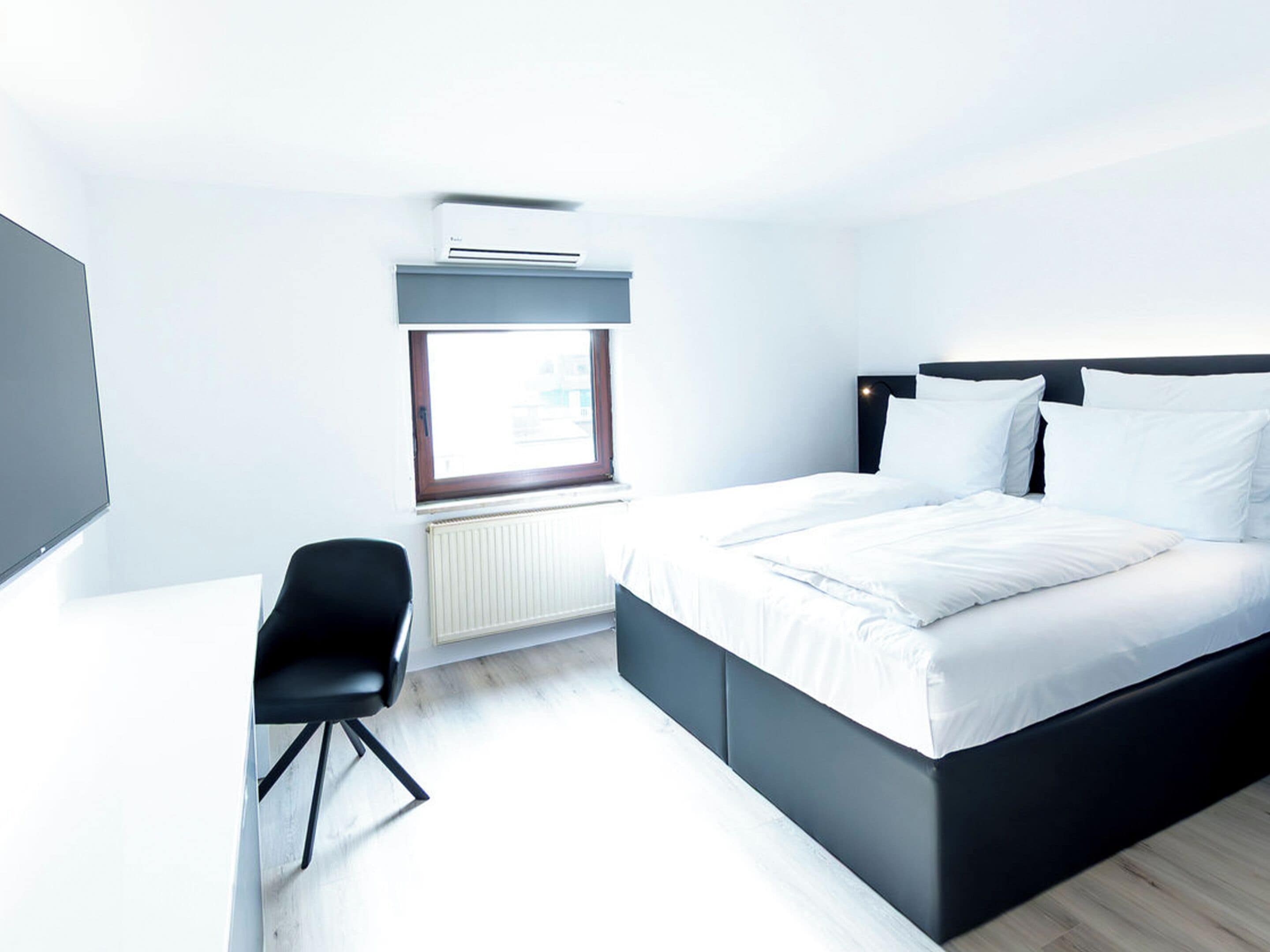 Una habitación de hotel moderna con cama, escritorio, silla, ventana y aire acondicionado.
