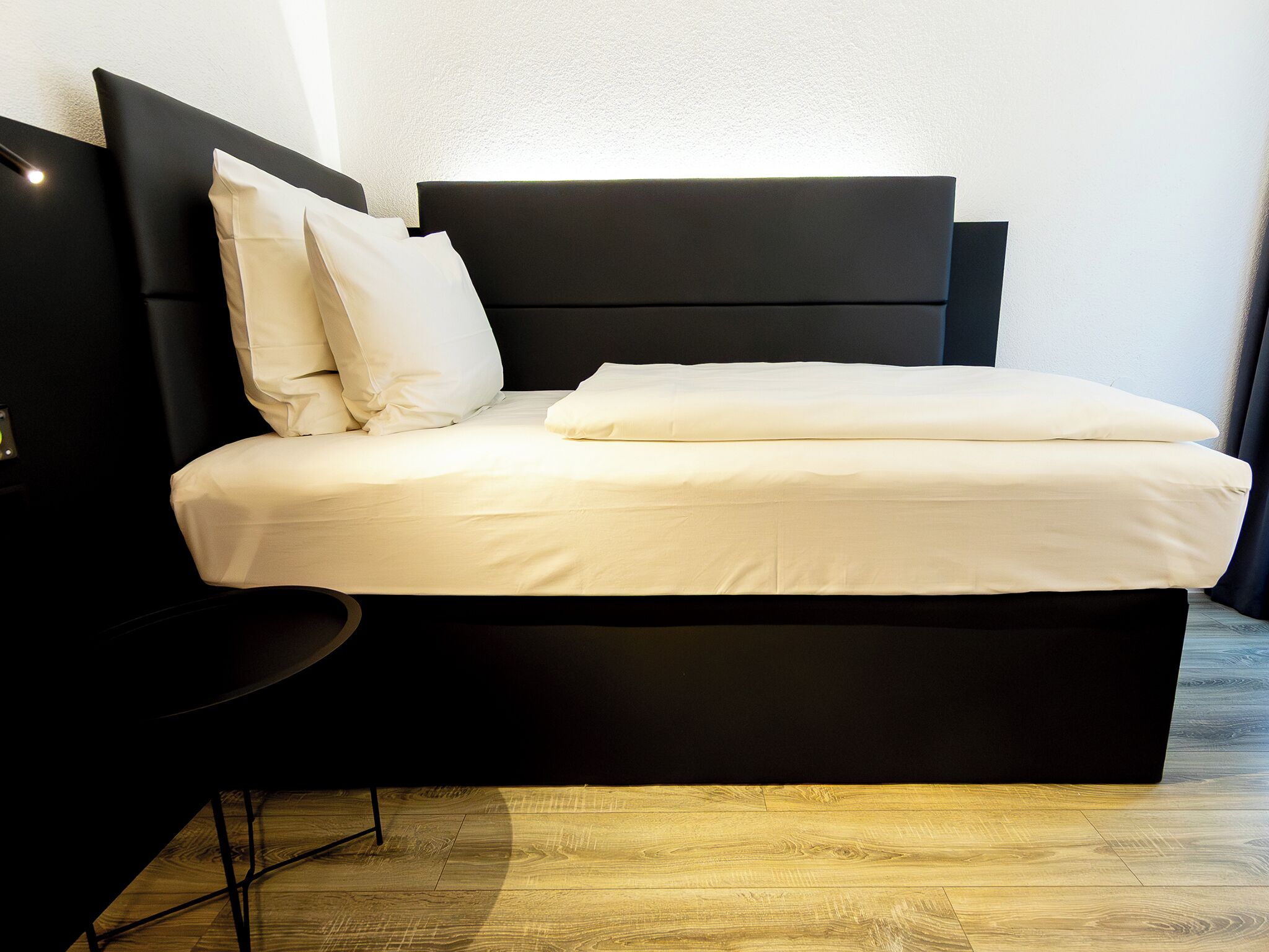 Un dormitorio moderno con cabecera negra, ropa de cama blanca y suelo de madera.