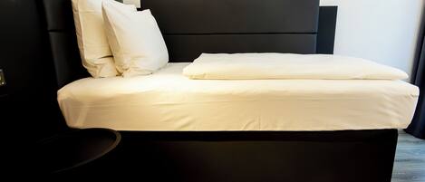 Un dormitorio moderno con cabecera negra, ropa de cama blanca y suelo de madera.