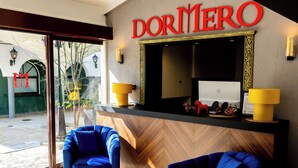 A hotel reception area with a large mirror, two blue chairs, and a 'Dormitorio' sign. - DORMERO Hotel Aalen (Aalen)
