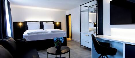 Una habitación de hotel moderna con cama, escritorio, silla, una pequeña mesa con un florero y un espejo grande.