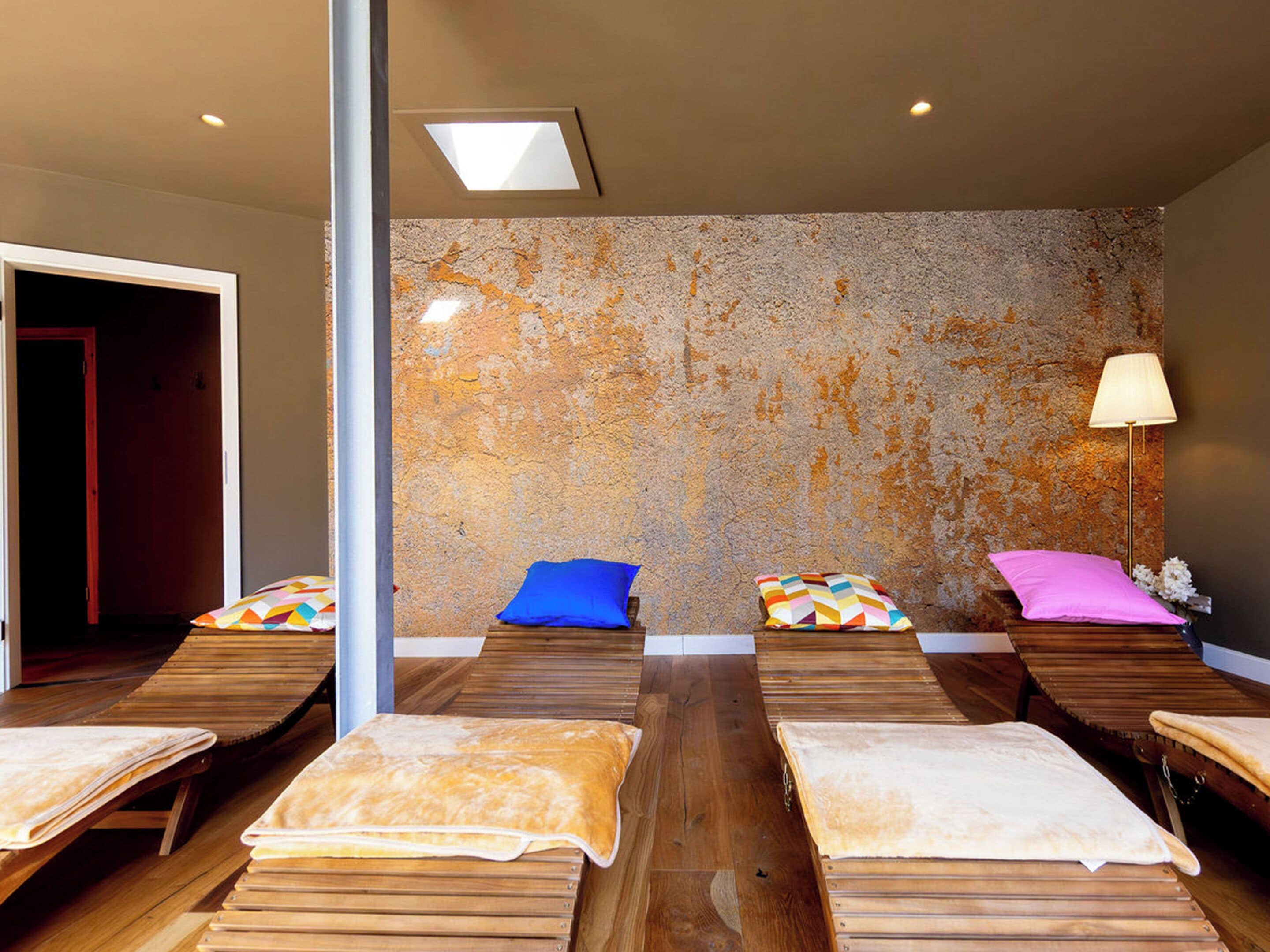 A room with wooden benches, colorful pillows, a stone wall, and a ceiling light.