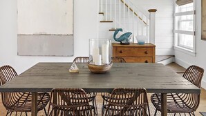 A dining area with a wooden table, wicker chairs, a glass candle holder, and a decorative bird sculpture. - Edgartown Village Home w/ Pool. 
4bdrm / 3.5bth (Edgartown)