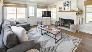 A modern living room with a sofa, coffee table, fireplace, and large windows. - Edgartown Village Home w/ Pool. 
4bdrm / 3.5bth (Edgartown)