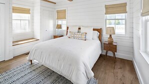 A bedroom with a large bed, wooden beams, white walls, and a window with a blind. - Edgartown Village Home w/ Pool. 
4bdrm / 3.5bth (Edgartown)