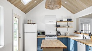 A modern kitchen with a wooden ceiling, white appliances, blue cabinets, and a central island. - Edgartown Village Home w/ Pool. 
4bdrm / 3.5bth (Edgartown)