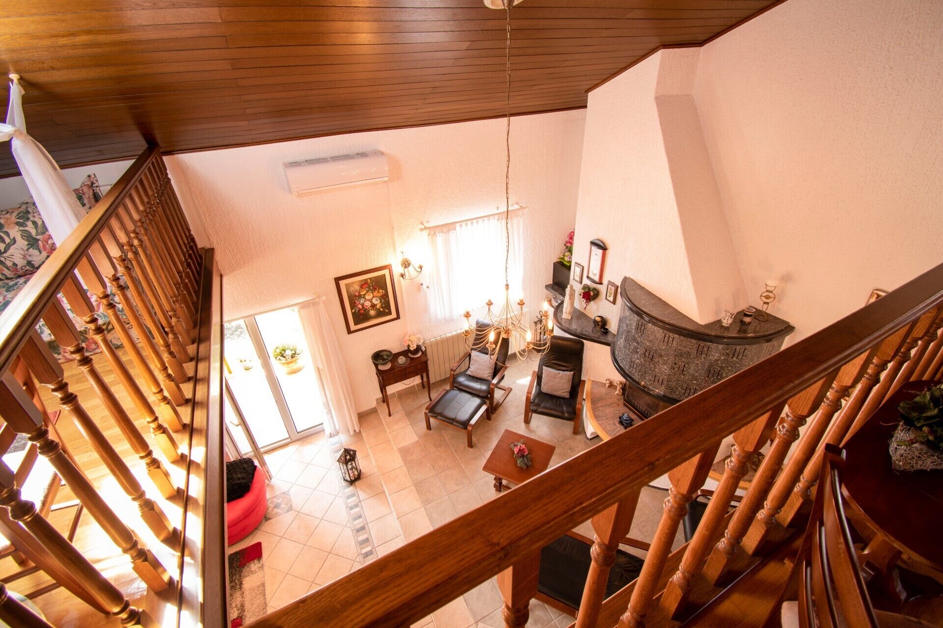 A spacious living area with a high ceiling, a fireplace, and a staircase with wooden railings.