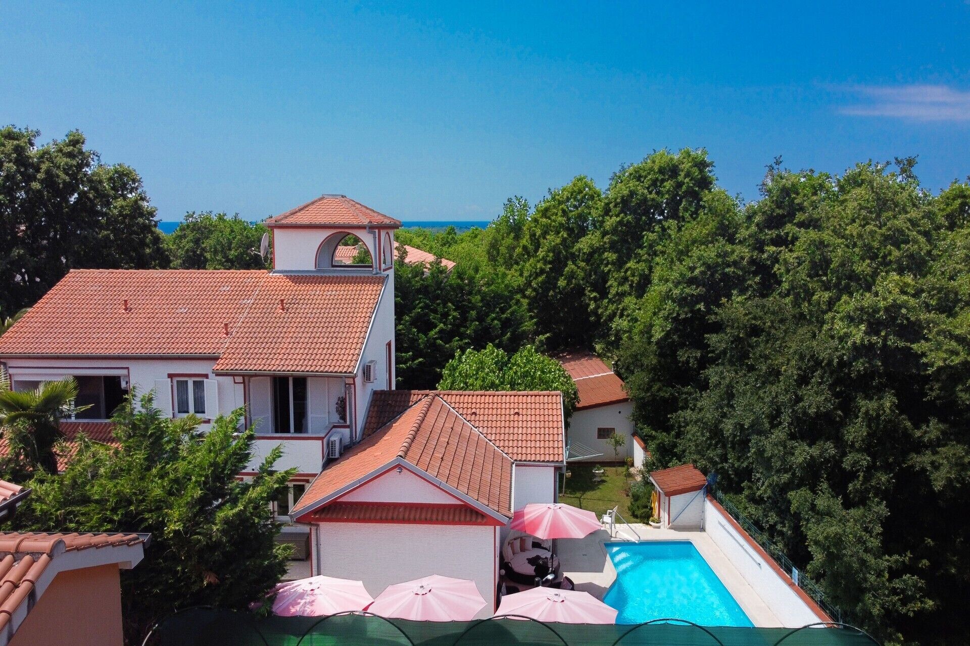 A residential area with a swimming pool, a bell tower, and a view of the sea.