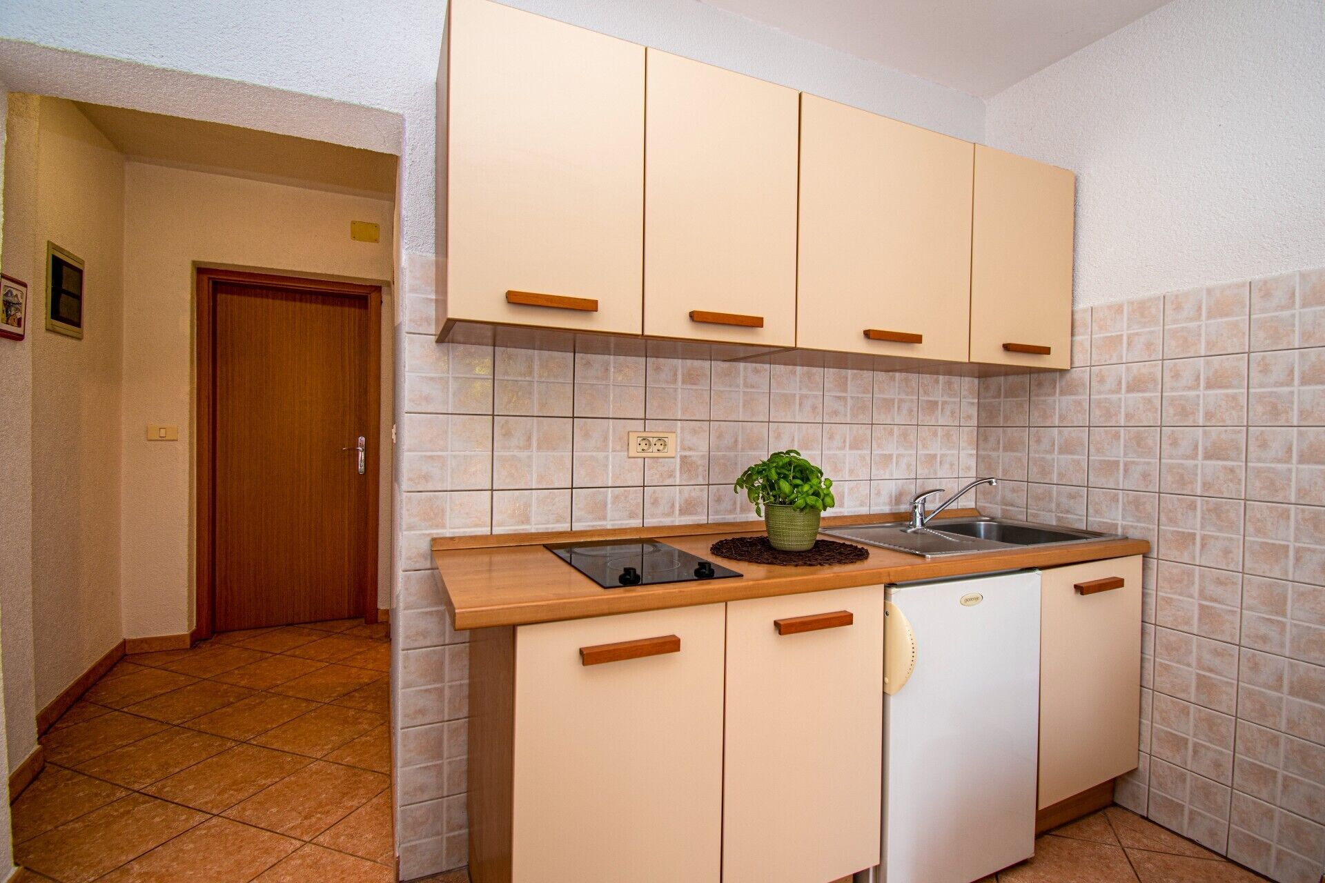 A compact kitchen with beige cabinets, a built-in sink, and a small refrigerator.