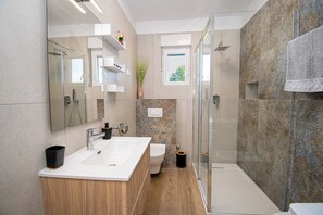 A modern bathroom with a glass shower enclosure, a double sink vanity, and a toilet.