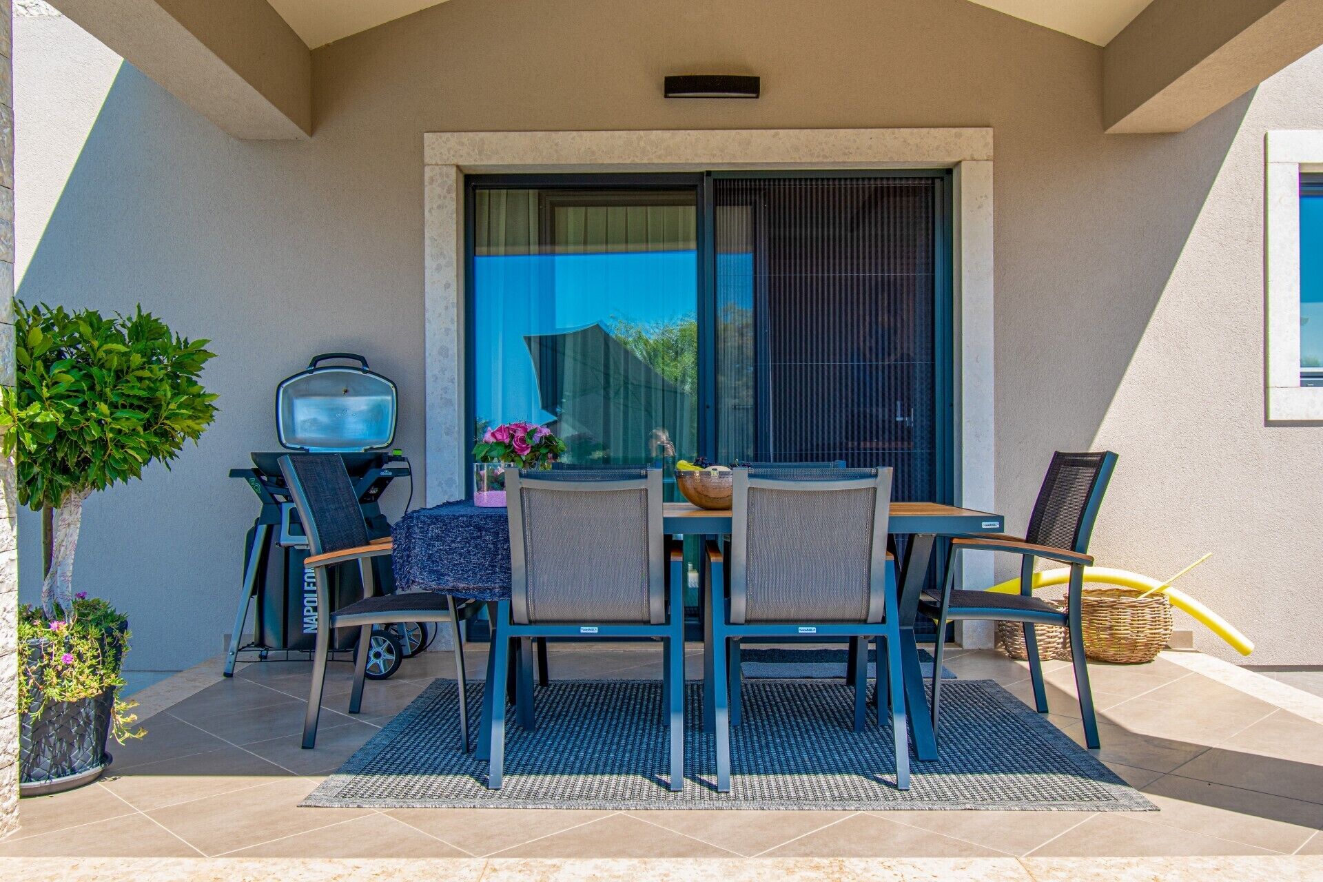 An outdoor patio with a table and chairs, a grill, and a potted plant.