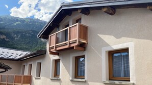 A building with a balcony, multiple windows, and a mountain backdrop.