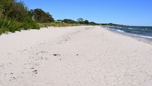 A wide, sandy beach with gentle waves, surrounded by greenery and a clear blue sky. - Cozy house in small village near the sea (Skåne län)