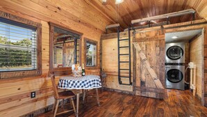 L’intérieur d’une cabane en bois, avec une table à manger, des chaises, une échelle et un lave-linge.