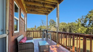 Une terrasse en bois, dotée de meubles en osier et d’une table, donnant sur une zone verdoyante.