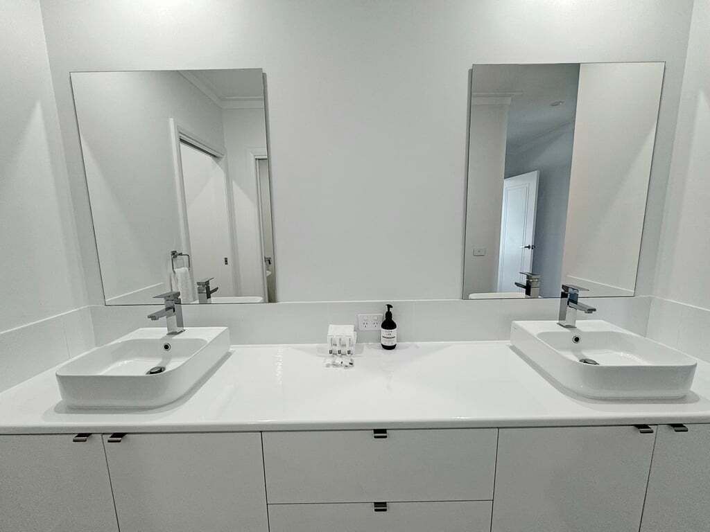 Une salle de bain moderne avec deux lavabos, un miroir et un flacon de savon pour les mains.