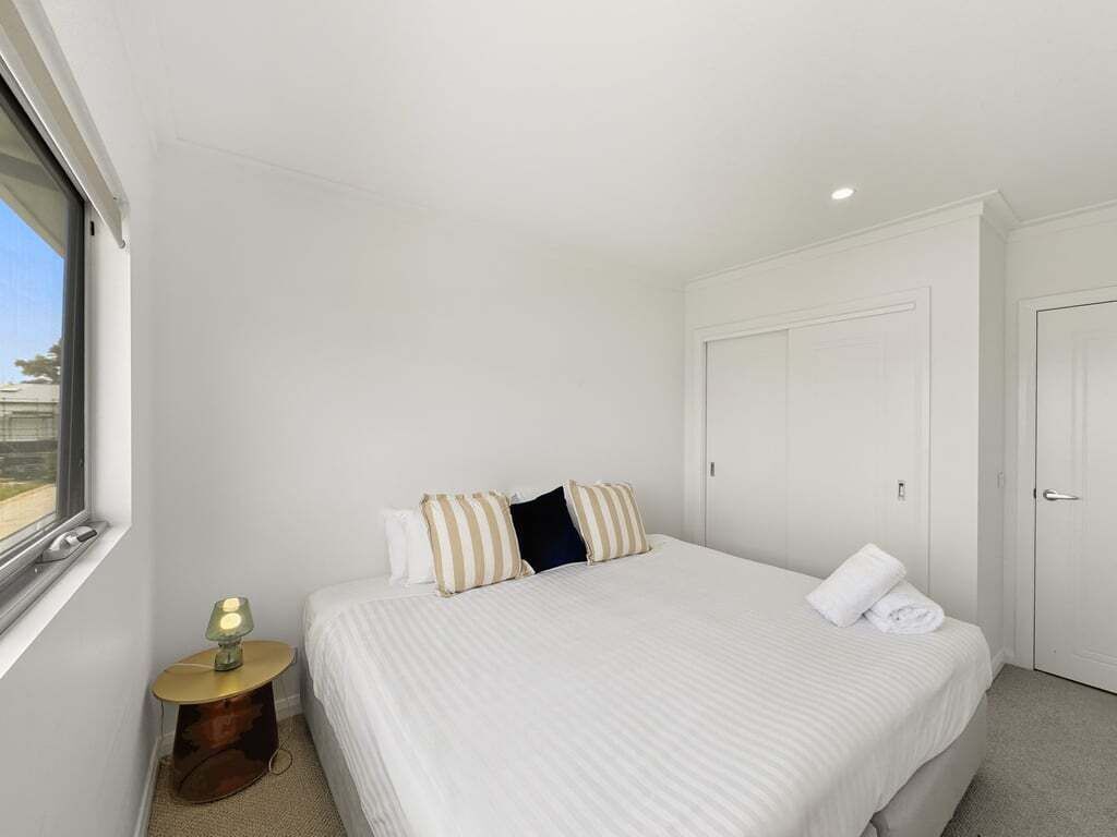 Een slaapkamer met een groot bed, een nachtkastje met een lamp en een kledingkast.