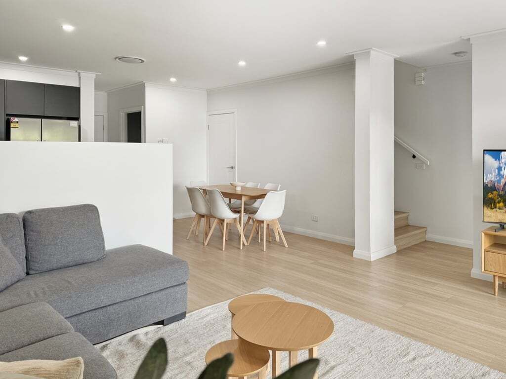 Una sala moderna con un sofá gris, una mesa de centro de madera y un comedor con una mesa y sillas blancas.