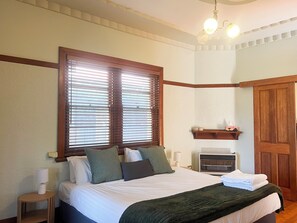 A neatly made bed with a green blanket, a bedside lamp, and a window with wooden blinds. - Beautiful home in a prime location! (Wagga Wagga)