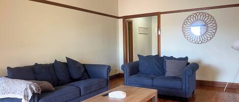 A living room with two dark blue sofas, a wooden coffee table, and a mirror on the wall.