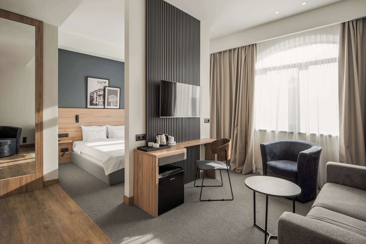 A modern hotel room with a bed, a desk with a chair, a small table, and a sofa.