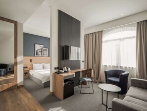 Ein modernes Hotelzimmer mit einem Bett, einem Schreibtisch mit Stuhl, einem kleinen Tisch und einer Couch.