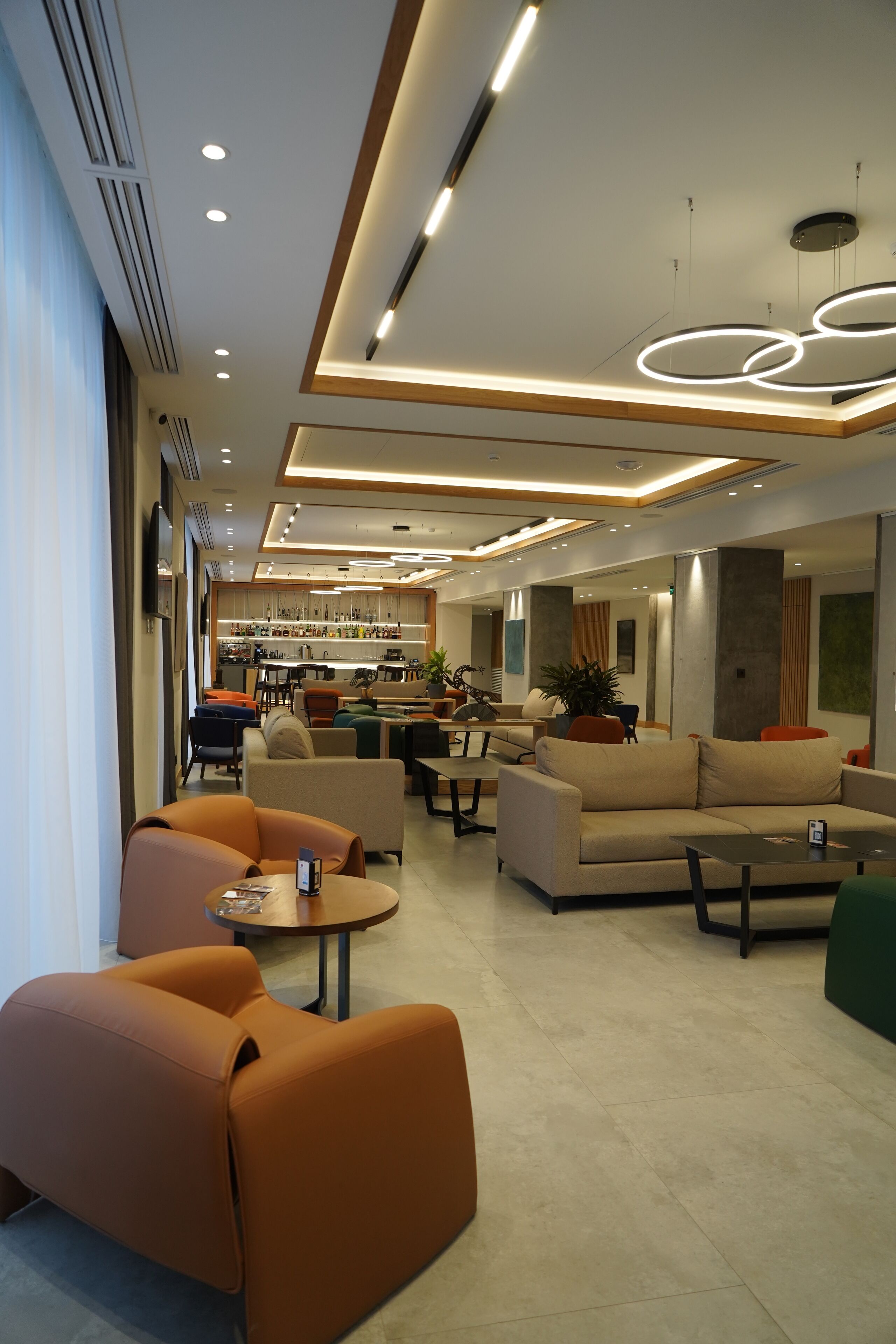 A modern hotel lobby with a bar area, seating arrangements, and a kitchen in the background.