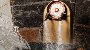 Ein Wasserspeier mit einem goldenen Ausguss und einer schwarzen Becken, vor einer Ziegelwand.