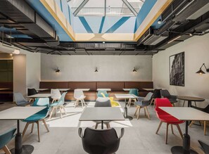 Ein modernes Interieur mit einer zentralen Sitzecke, Tischen und Stühlen darum herum.