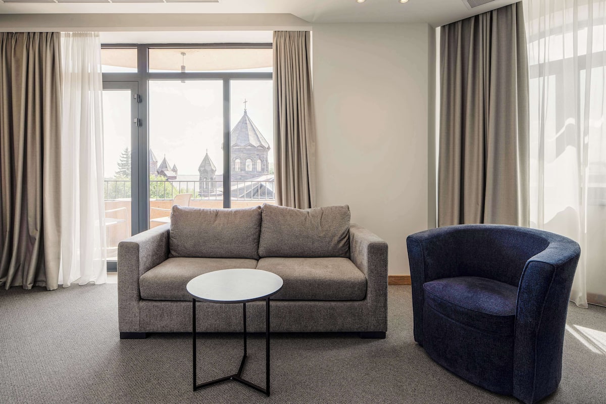 A modern hotel room with a grey sofa, a blue armchair, and a small round table.