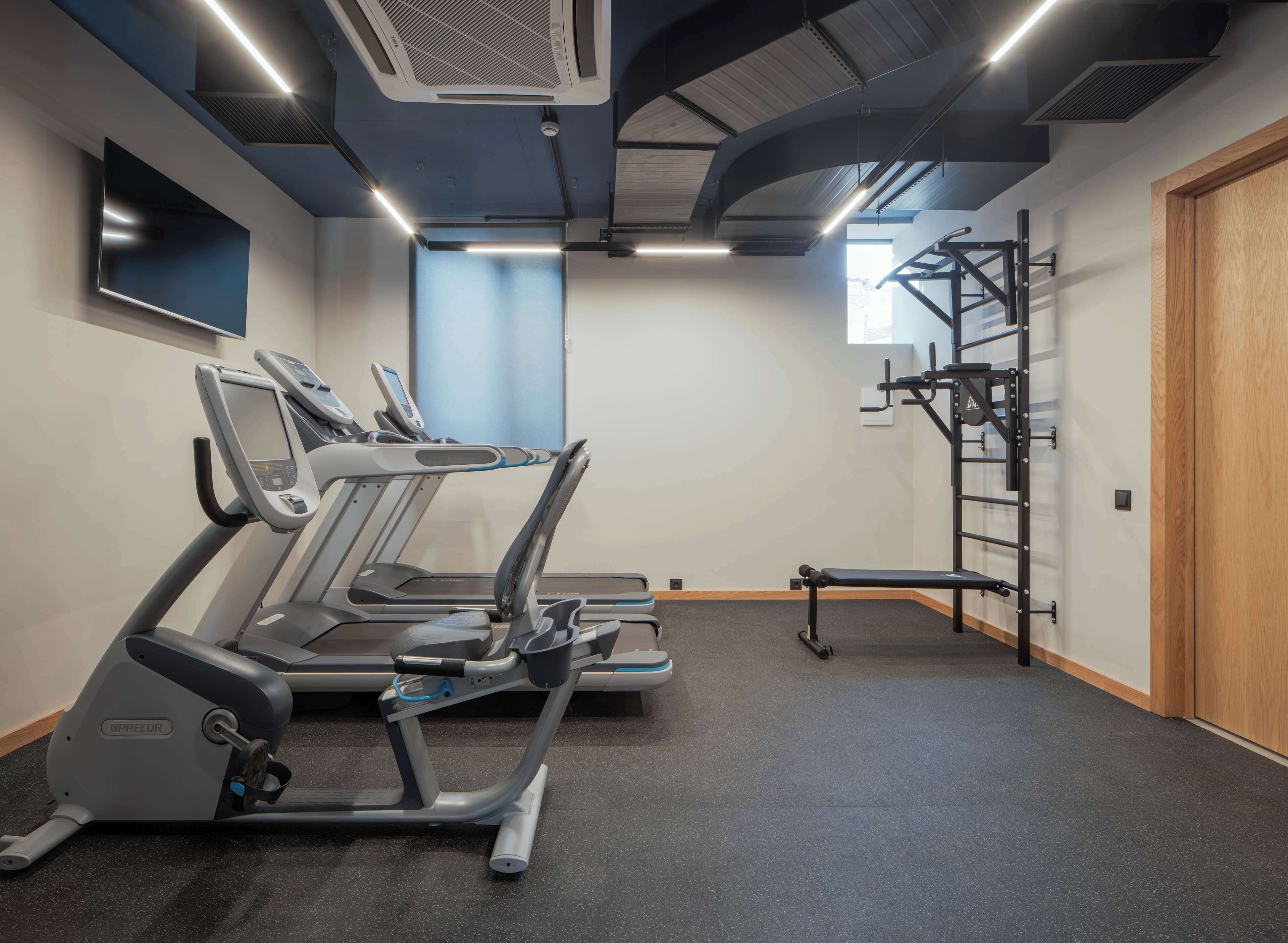 Een sportschool met loopbanden, een halterrek en een houten deur.