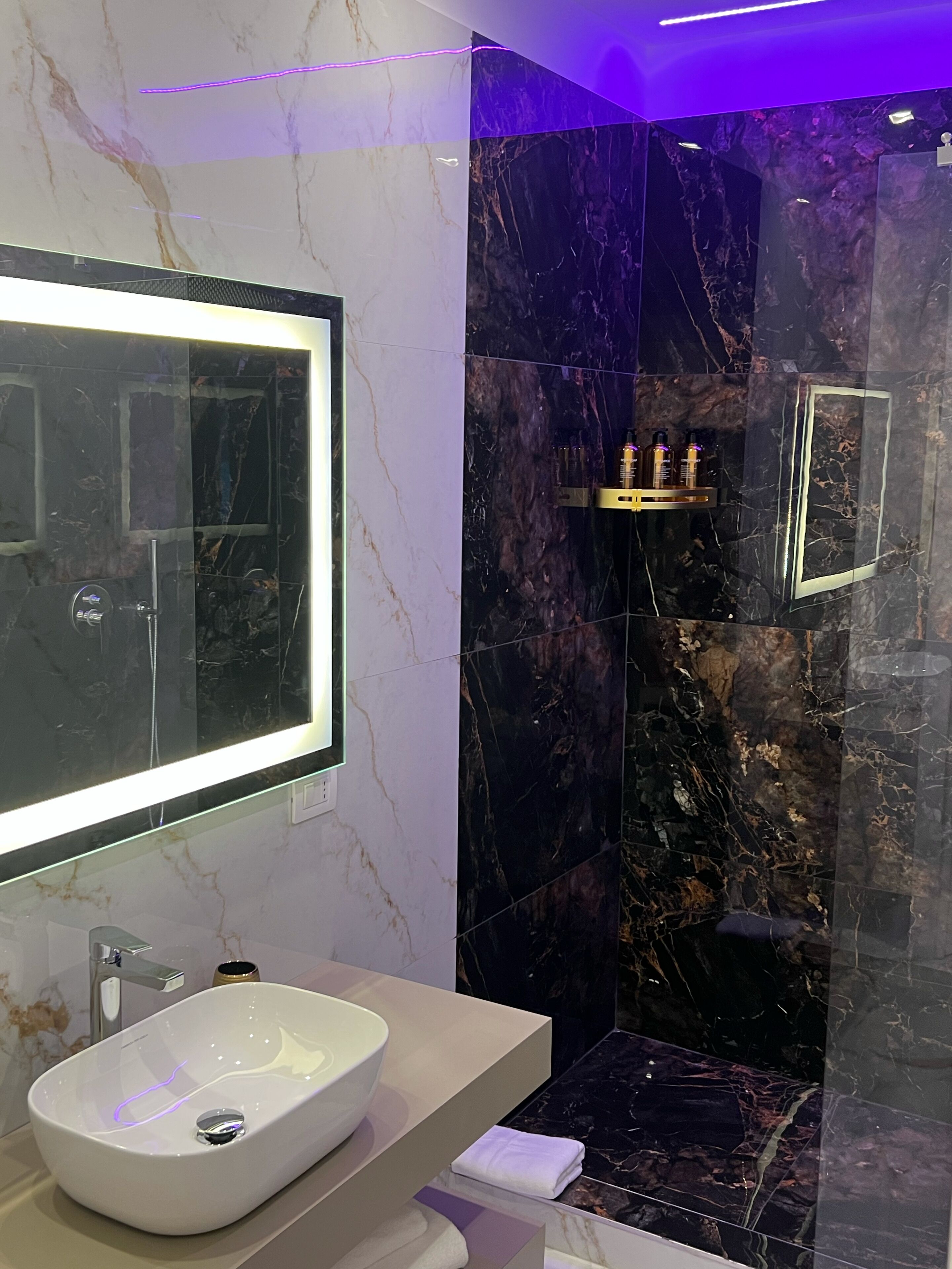Une salle de bain moderne avec un grand miroir, un lavabo blanc et une douche séparée par une paroi de verre.