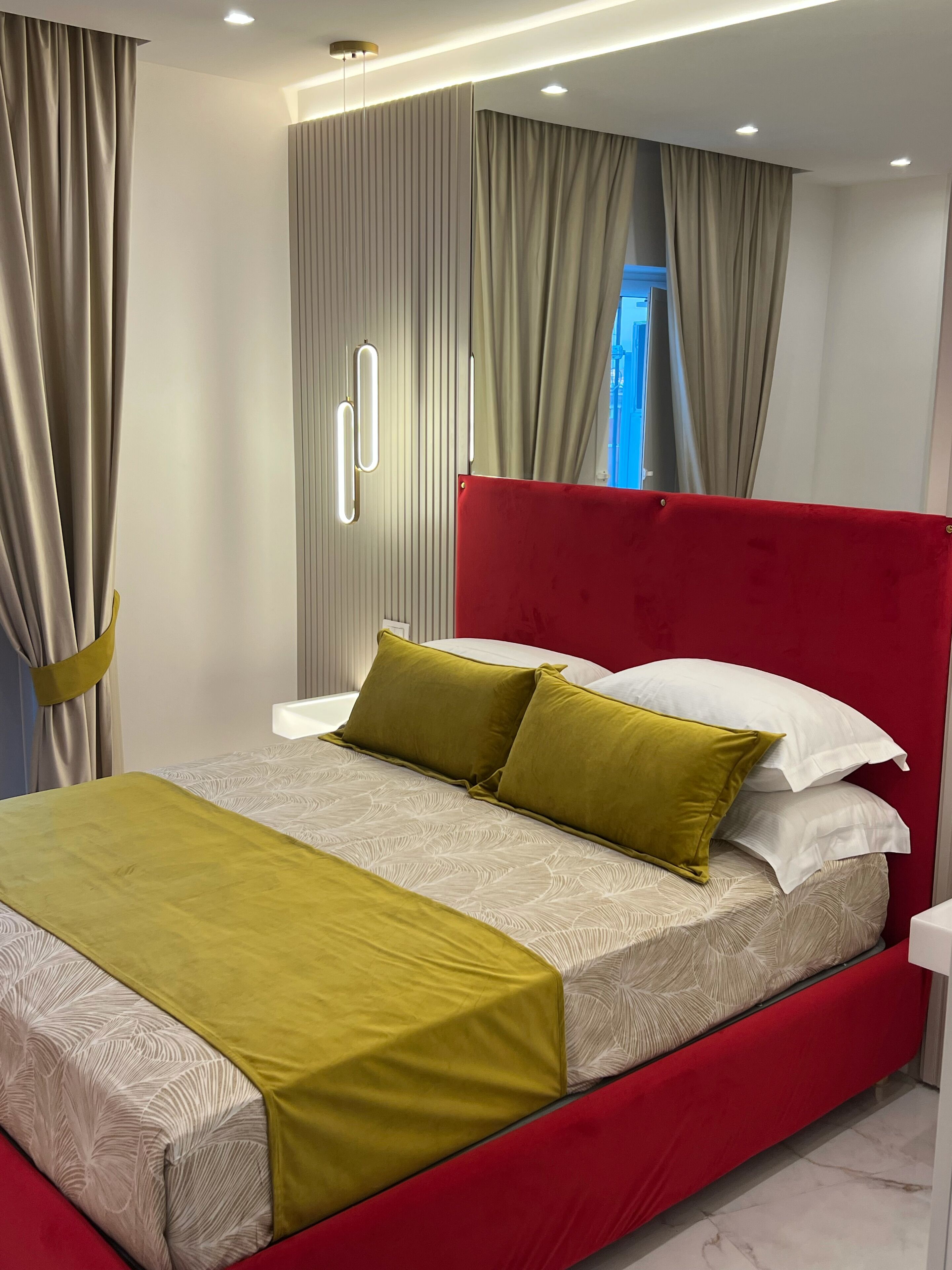 A modern bedroom with a red headboard, a bed with a patterned bedspread, and a window with curtains.