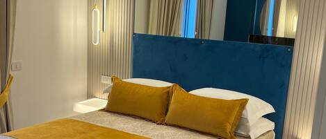 A modern bedroom with a blue headboard, a large bed with white and yellow bedding, and a marble floor.